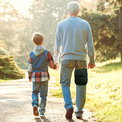 An elderly man wearing an extra large wearable ice pack around his thigh for fibromyalgia relief while walking with his grandson.