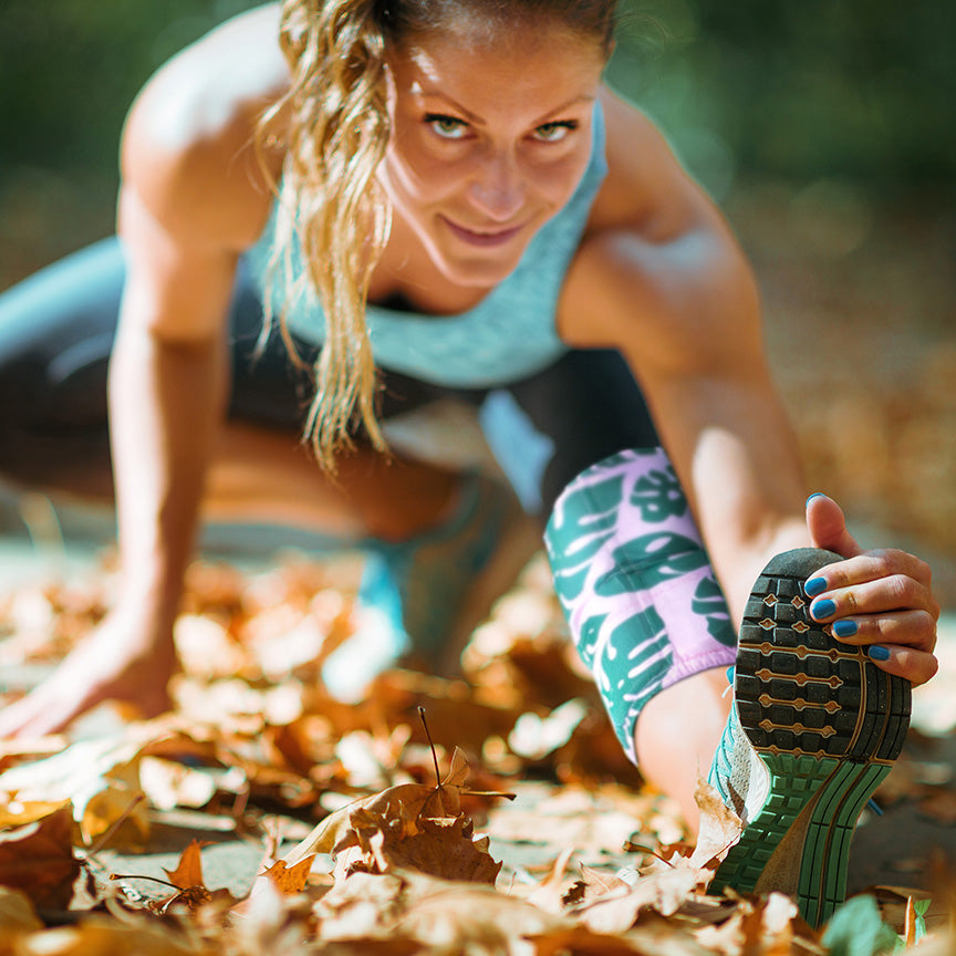 A woman stretching and smiling while wearing a HurtSkurt wearable ice pack for leg cramps.