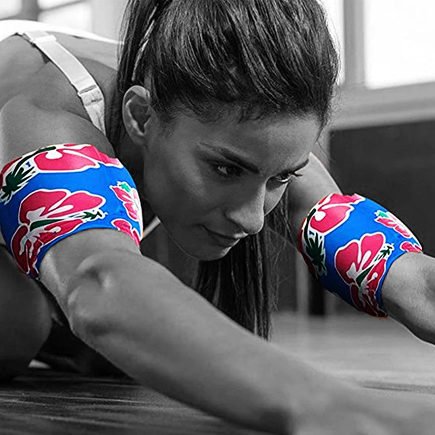 A black and white photo of a woman completing pre-workout stretches while wearing two tropical patterened HurtSkurt wearable ice packs on her biceps for workout recovery.