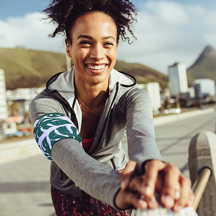 A woman in athletic wear is smiling while stretching and wearing a flor patterned HurtSkurt cold pack for workout recovery.