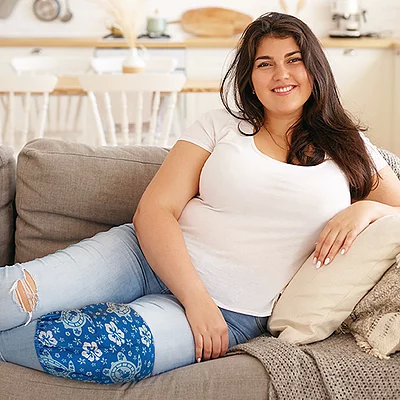 A woman resting on a sofa while wearing an extra large ice pack for knee pain relief.