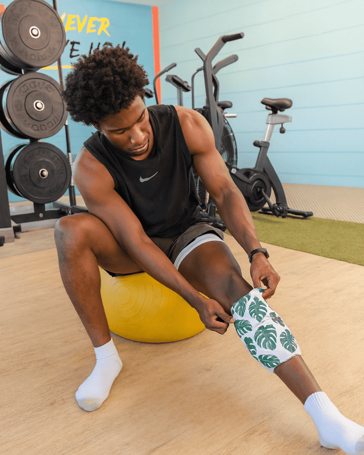 Man in a gym zipping the HurtSkurt Large wearable ice pack around his knee